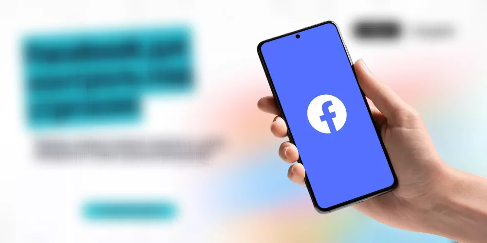 A hand holds a smartphone displaying the Facebook logo on a blue screen, with blurred text and graphics in the background.